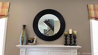 Front view of the round wall mirror on wall above mantel with items around it.