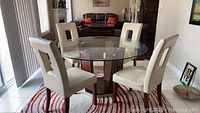 Photo showing square glass top dining table and four cream faux leather chairs in living room area