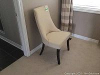 Side view of beige upholstered chair with dark wooden legs showing height and curvature of backrest.