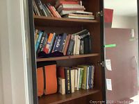 Books stored in a cabinet showing a variety of titles with some raised in front of an orange bag