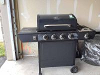 Full view of the black Backyard Grill propane BBQ with four burner control knobs and attached side burner, standing on wheels.