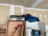 Three Locker Dome tent in storage bag and two folded tarps on top of cabinets against a garage wall.