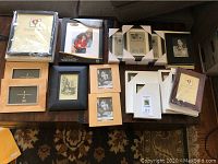 Lot of various new photo frames from Crate and Barrel and IKEA, assorted sizes, styles, and colors (wood natural, black, white). Frames are new, some still wrapped, laid out on a wooden surface and couch.