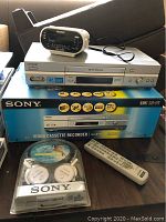Sony VHS player on top of its original box with Sony branded remote and headphones in original packaging placed beside it. Also visible is a Sony digital alarm clock.