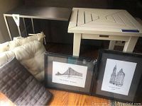 Full lot view showing wooden table, metal side table, two chair cushions, gray pillow cover, and two framed pen and ink artworks in black frames