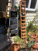 Black Rubbermaid foldable step stool standing next to wooden ladder-style shelf outdoors.