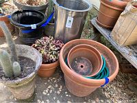 Photo showing the terra cotta pots, one with leafy plant, coiled green hose inside a large pot, and stainless steel container
