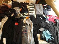 Wide view of assorted items spread on bed: jackets, shirts, underwear packs, sports bras, base layers