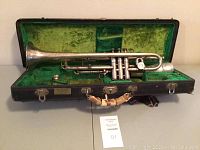 Full view of silver plated trumpet seated in open black hard case with green plush lining