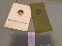 Two official inaugural programs laid flat on a surface, showing titles and covers. One is cream color with gold embossed eagle and titled 'Official Inaugural Program', the other is green with a seal and a handwritten signature of Governor Reagan.