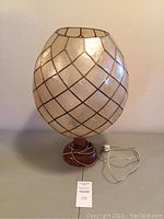 Front view of the lamp showing the capiz shell lampshade with geometric pattern, wooden base, old wiring, and rotary switch.