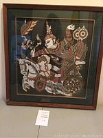 Full front view of the framed painting showing chariot, demon, driver, and horses on dark green silk.