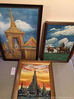 Photo showing all three framed paintings placed leaning on a wall, depicting the King's coronation throne, plowing buffalo, and Temple of the Dawn.