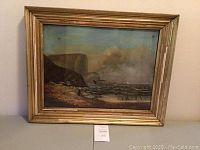 Framed painting showing coastal seascape with cliffs, waves, and boats, housed in a gold-toned wooden frame with some damage.