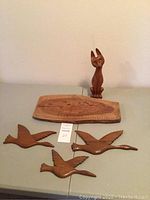 Photo shows carved wooden cat statue, carved wooden plaque, and three carved birds together on table.