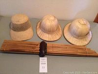 Photo showing the Khaen mouth organ placed horizontally beneath three bamboo woven hats on a flat surface against a wall.