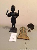 Front view of the Tibetan heavy metal Guan Yin statue with 8 arms and 4 faces, small brass peacock, and wooden plaque arranged on a table.