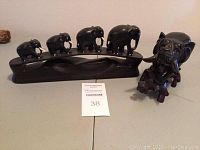 Front view of four carved wooden elephants on a bridge base and a single separated carved wooden elephant figurine.