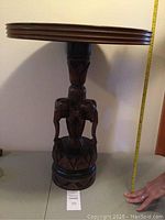 Full view of the table showing carved elephant pedestal and measuring tape indicating approximate height of 25 inches.