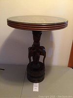 Full front view of the wood round table showing the carved elephant pedestal and the circular top.
