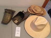 Photo detailing two brass stirrups and two straw hats placed on a light-colored surface.