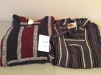 Two cotton hoodies folded on a surface showing striped patterns in maroon, black, and white and another with purple and black stripes.