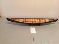 Full view of wooden model canoe with dark green exterior and exposed ribbing inside, displayed on flat surface.
