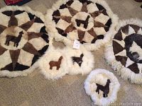 All six alpaca hide circular decorative hangings laid out on carpet, showing three large pieces with geometric design and alpaca silhouette and three smaller pieces with alpaca silhouettes.