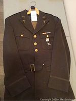 Front view of WWII U.S. Army uniform jacket on hanger showing overall condition, buttons, and belt.