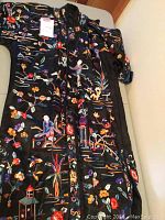 Full view of coat laid flat showing embroidered designs all over, including figures, birds, flowers, and pagodas.