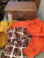 Vintage brown Stream Guard suitcase with metal corners, clasps, and handle, placed behind clothing items