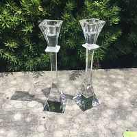 Two clear crystal Nachtmann candle holders standing upright outdoors against green foliage showing sides and square bases.