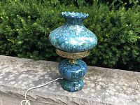 Lamp assembled and powered by cord shown on stone surface outdoors with greenery in background