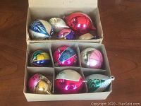 Top view of cardboard box containing eleven assorted vintage glass Christmas ornaments in multiple colors and shapes.