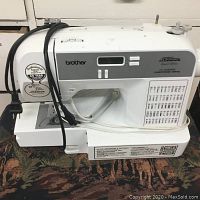 Front view of sewing machine with power cord and foot pedal on patterned surface.