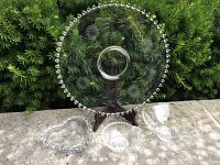 Large Cornflower plate with hobnail bead trim and floral etching on wooden stand alongside three smaller bowls on stone surface outdoors
