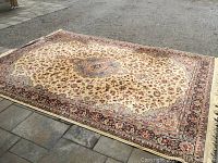 Full view of rectangular ivory rug with floral medallion pattern laid on pavement