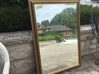 Full view of the large rectangular mirror leaning against a stone wall outside, showing its size and reflective surface.