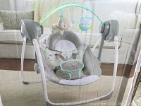 Front view of the assembled Ingenuity baby swing showing seat with toy bar and padded cover.