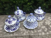 Set of four blue and white ceramic cups each with lid and saucer showing different floral and geometric patterns