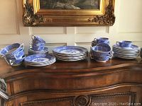 Full set displayed on wooden sideboard under painting showing stacks of plates and cups