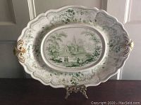 Full view of oval platter on display stand showing scalloped edge and gilt handles