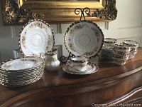 Full set displayed on sideboard with plates, cups, saucer stacks, creamer and serving plates