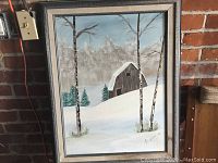 Framed winter landscape painting showing a snow-covered barn, surrounding birch trees, and pine trees in the background.