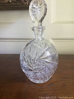 Clear crystal decanter with pinwheel cut pattern on the body and faceted stopper on top.