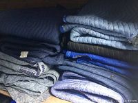 Stack of assorted packing blankets showing multiple folded blankets in blue and gray colors.