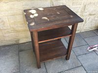 Front view of small dark wooden table with two lower shelves and rectangular inset top panel.