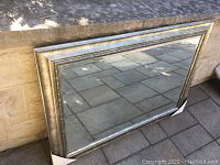 Full view of rectangular beveled glass mirror leaning against stone wall outdoors on patio before pickup.