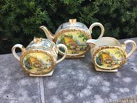 Full set front view of Sadler Crinoline Lady porcelain teapot, creamer, and covered sugar bowl with scenic and gold detailing.