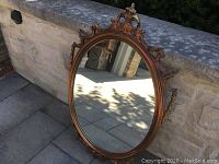 Full view of ornate oval mirror with bronze-toned frame showing decorative top with floral and scroll details.